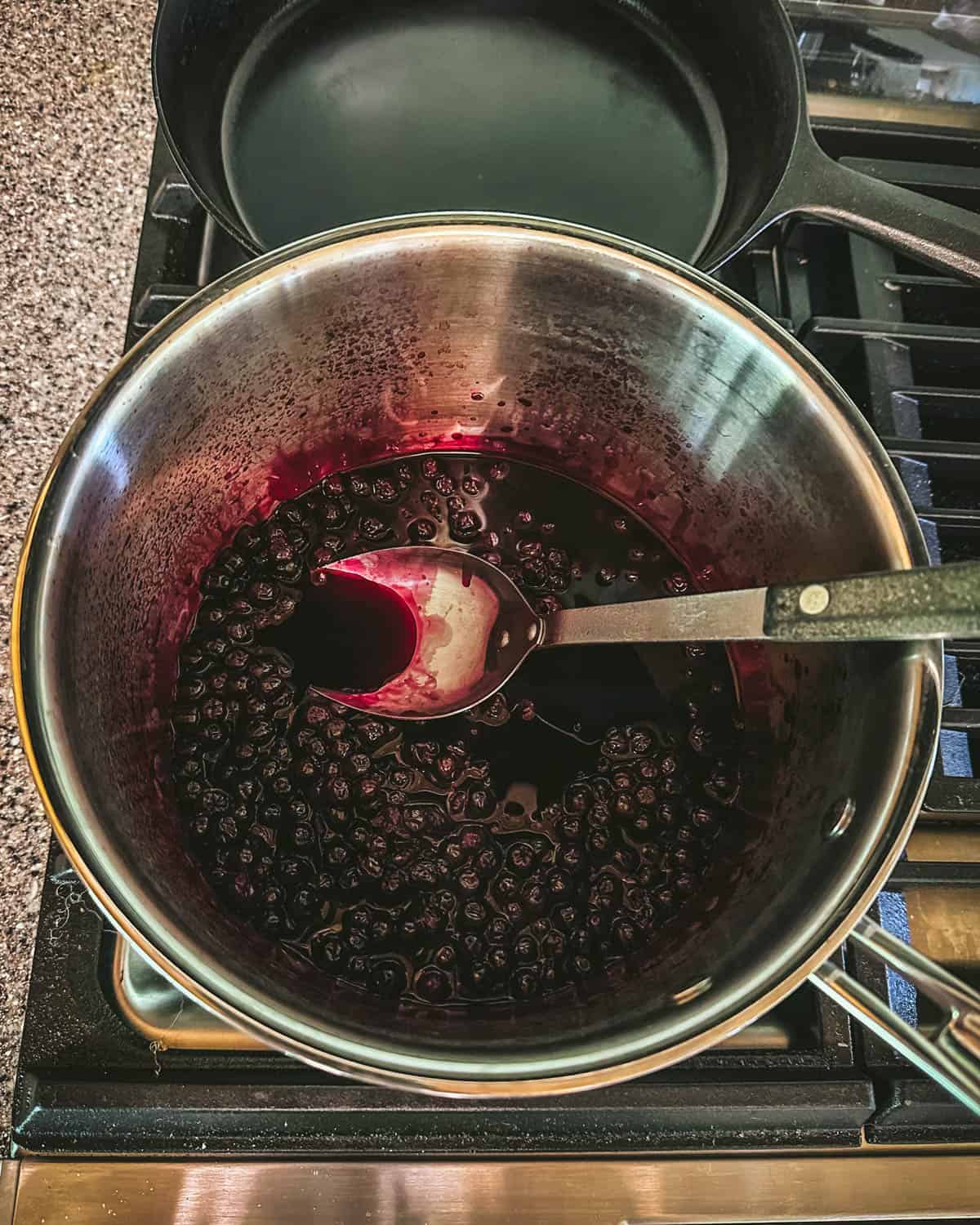 Aronia berry infusion cooling in a pot on a stove with a large long handled spoon in it. 