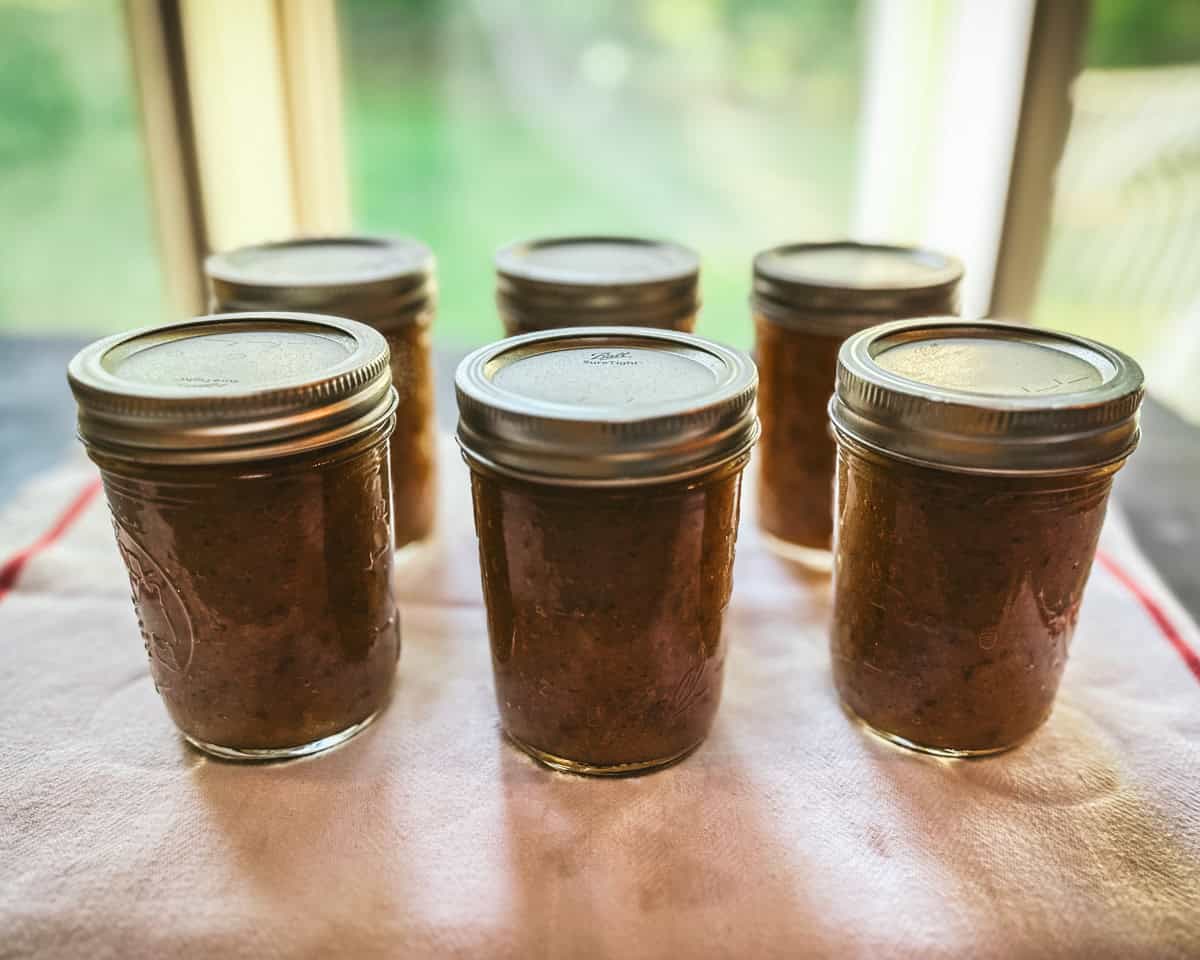 Canned jars of pear butter on a wood surface in front of a window with natural light. 