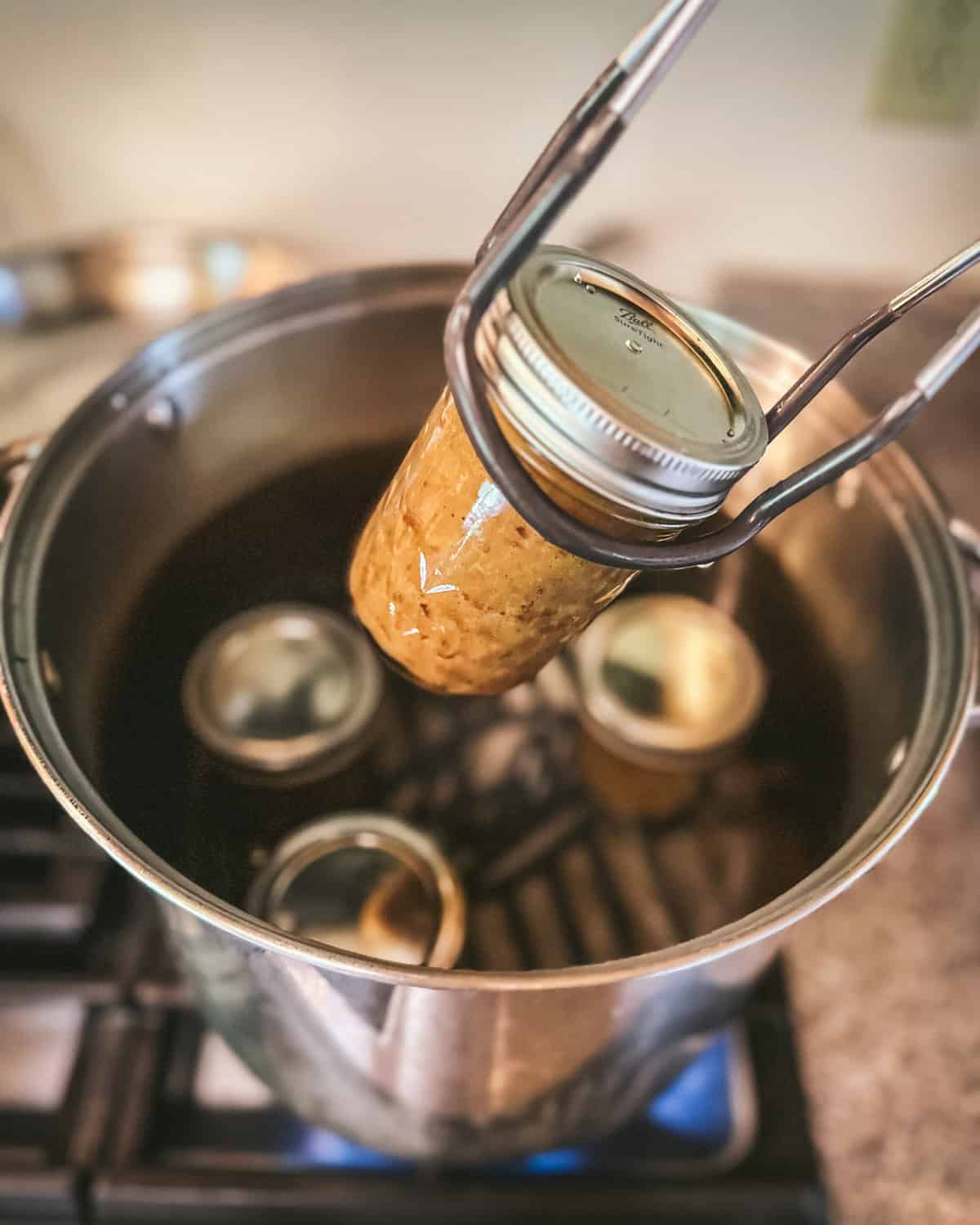 A jar lifter taking a jar of pear butter out of the canner. 