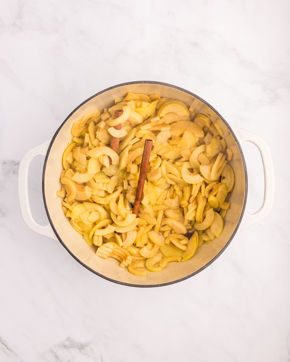 Cooked sliced apples in a white pot on a white counter, top view. 