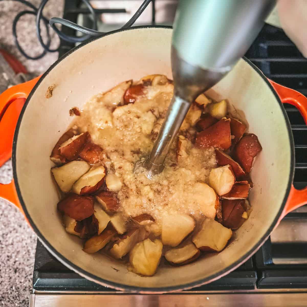 An immersion blender blending the cooked pears in the pot, top view. 