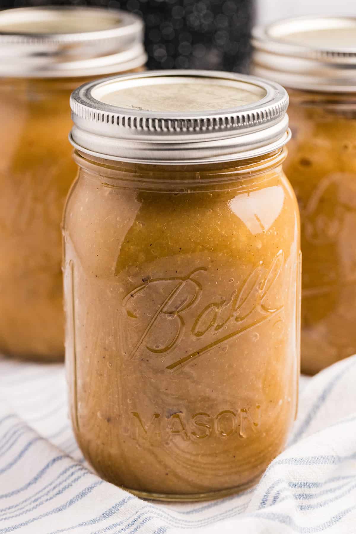 A jar of chunky applesauce cooling on a towel on the counter, with two others in the background. 