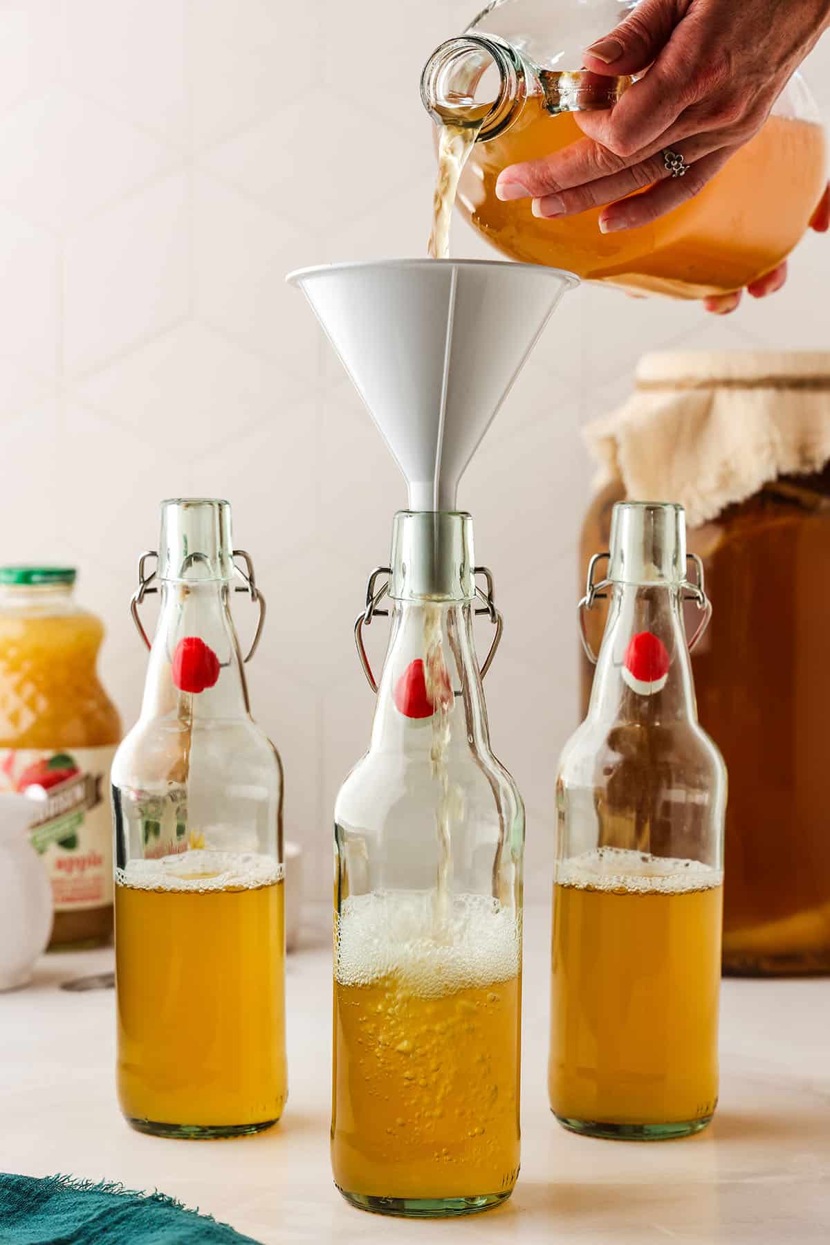 Flip top bottles half filled with kombucha, one with a funnel on it with kombucha pouring into it. 