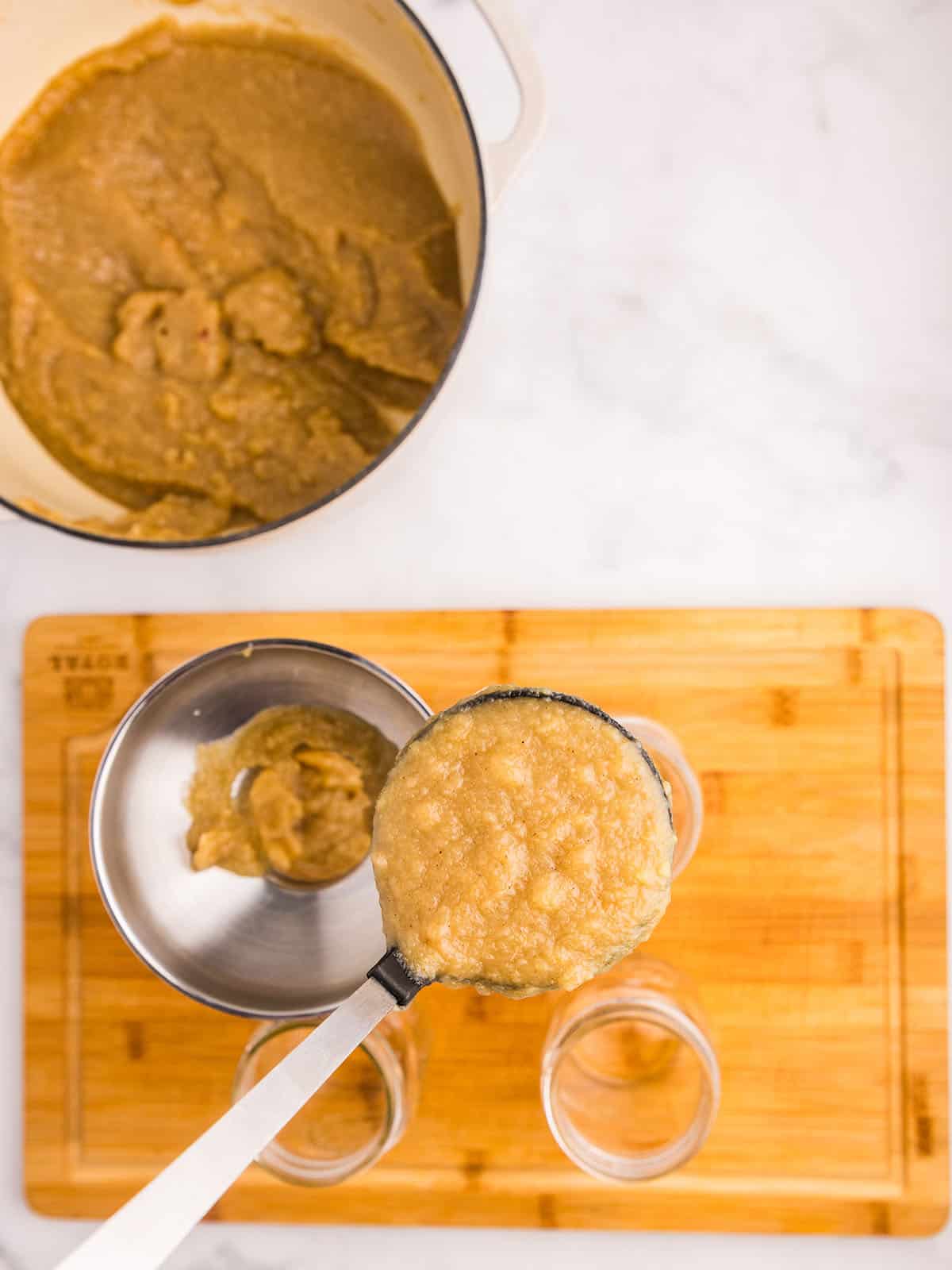 A ladle pouring homemade applesauce through a funnel into a canning jar, top view. 