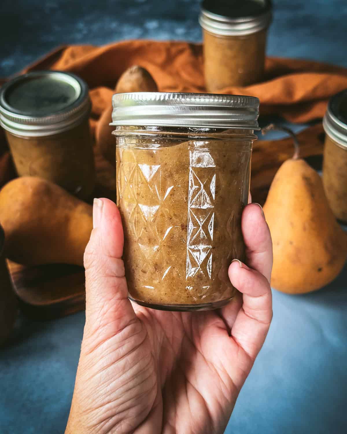 A hand holding up a jar of pear butter. 