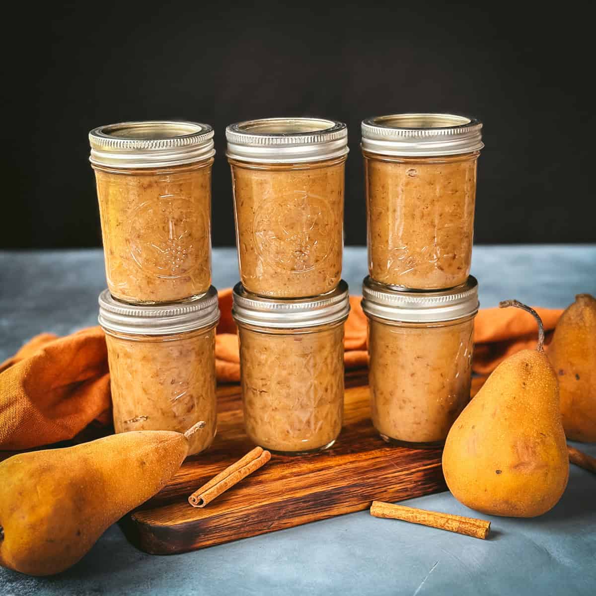 6 jars of pear butter on an orange cloth, with a whole pear and a cinnamon stick. 