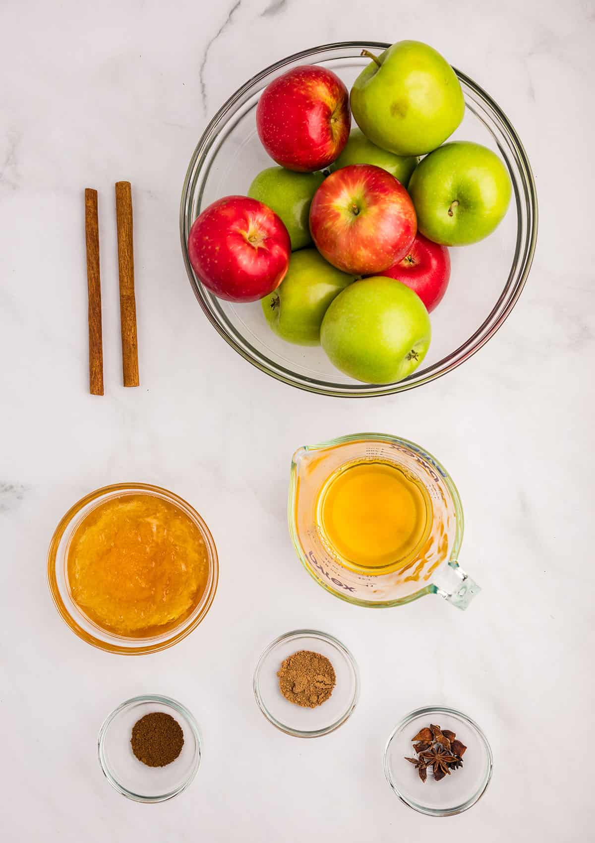 Bowls of ingredients for applesauce on a white counter, top view. 