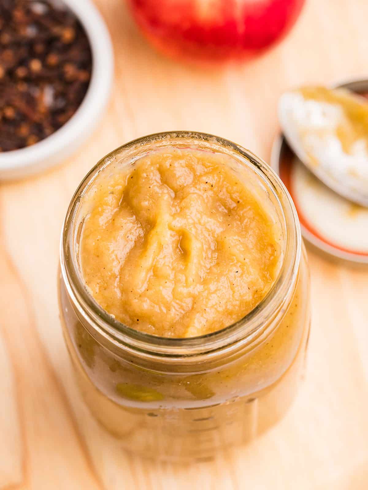 A jar of applesauce without a lid on a wood surface, top view.