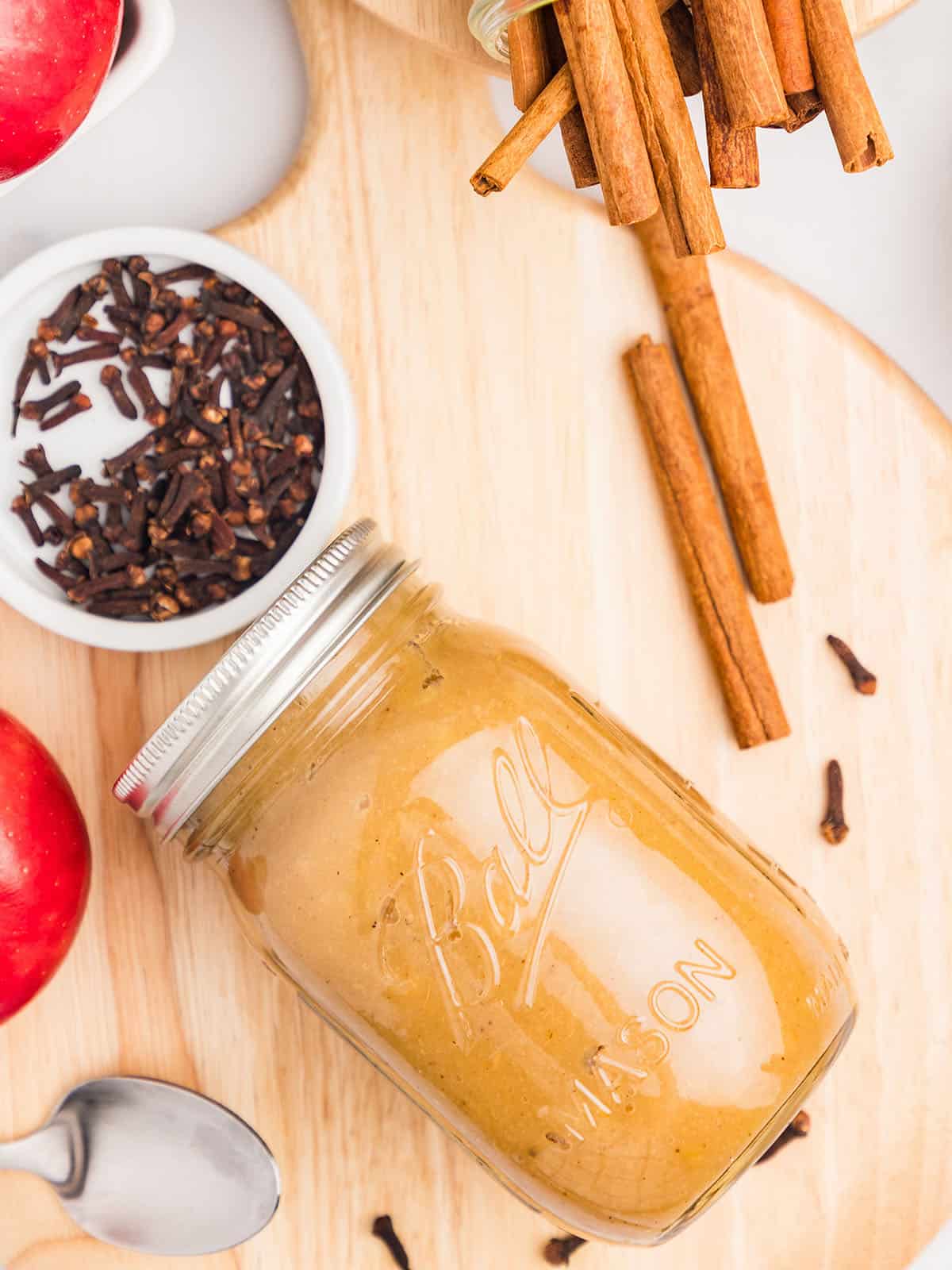 A jar of canned applesauce laying on its side, surrounded by fresh whole spices. 