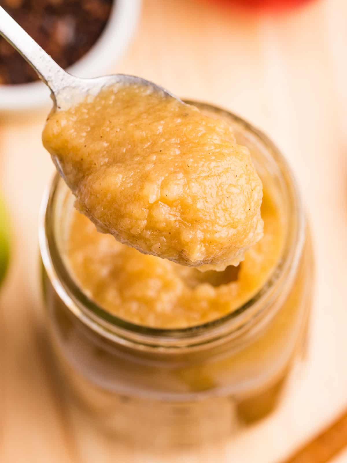 A spoon lifting spiced applesauce out of a jar, top view. 