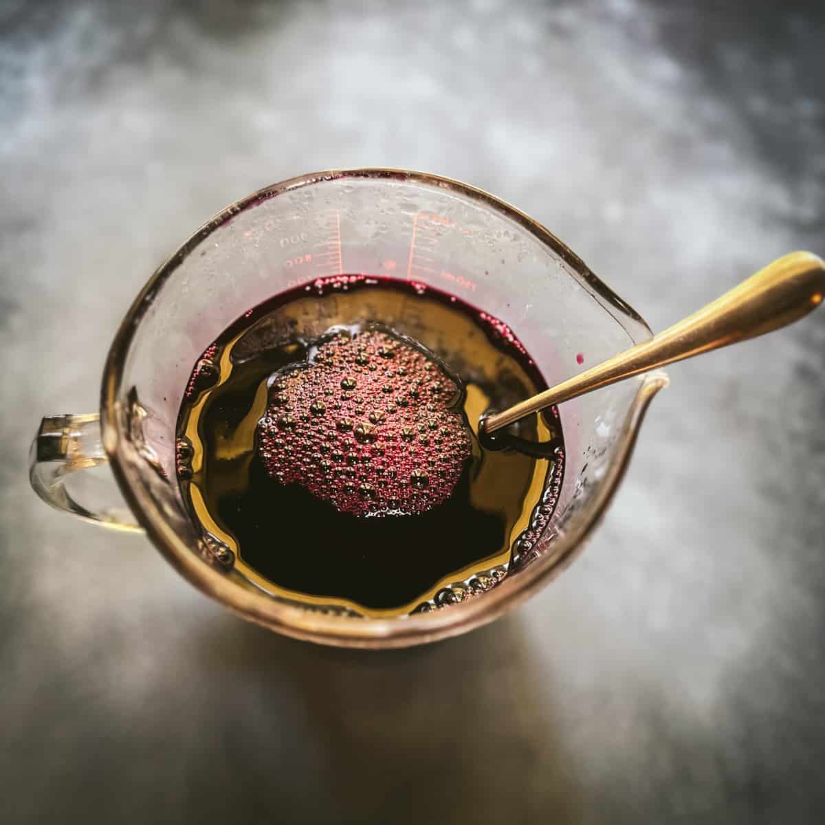 Aronia oxymel being stirred with a spoon in a pyrex pouring glass, top view. 