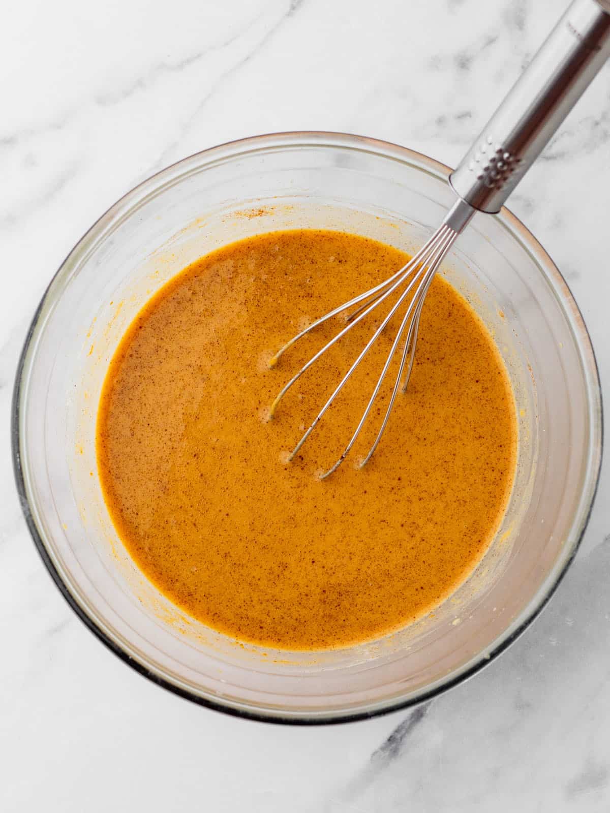 Pumpkin and spices added to the bowl with yeast mixture, making it orange. With a whisk in it. Top view. 