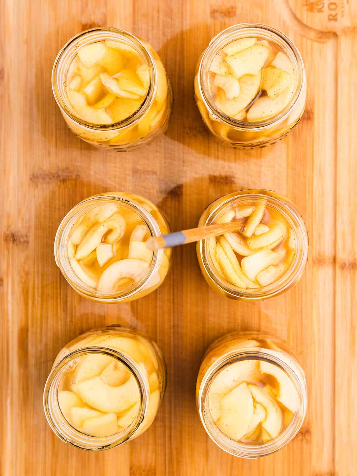 Filled jars with apple pie filling, no lids. On a wood surface, top view. 