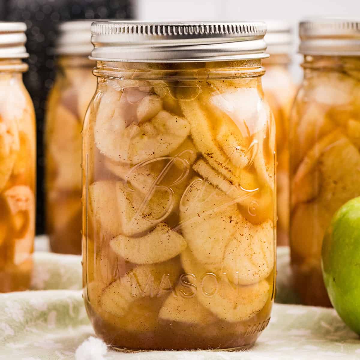 A jar of apple pie filling with several others in the background. 