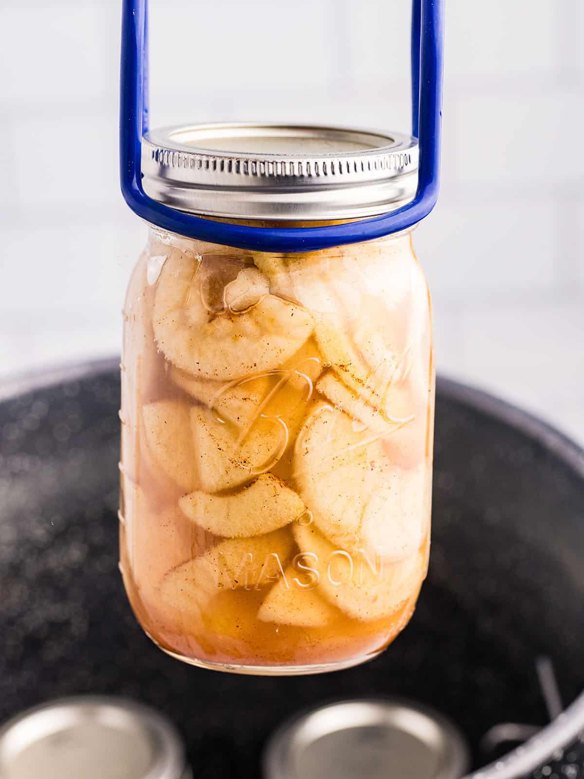 A jar of apple pie filling being lifted out of a canner with a jar lifter. 