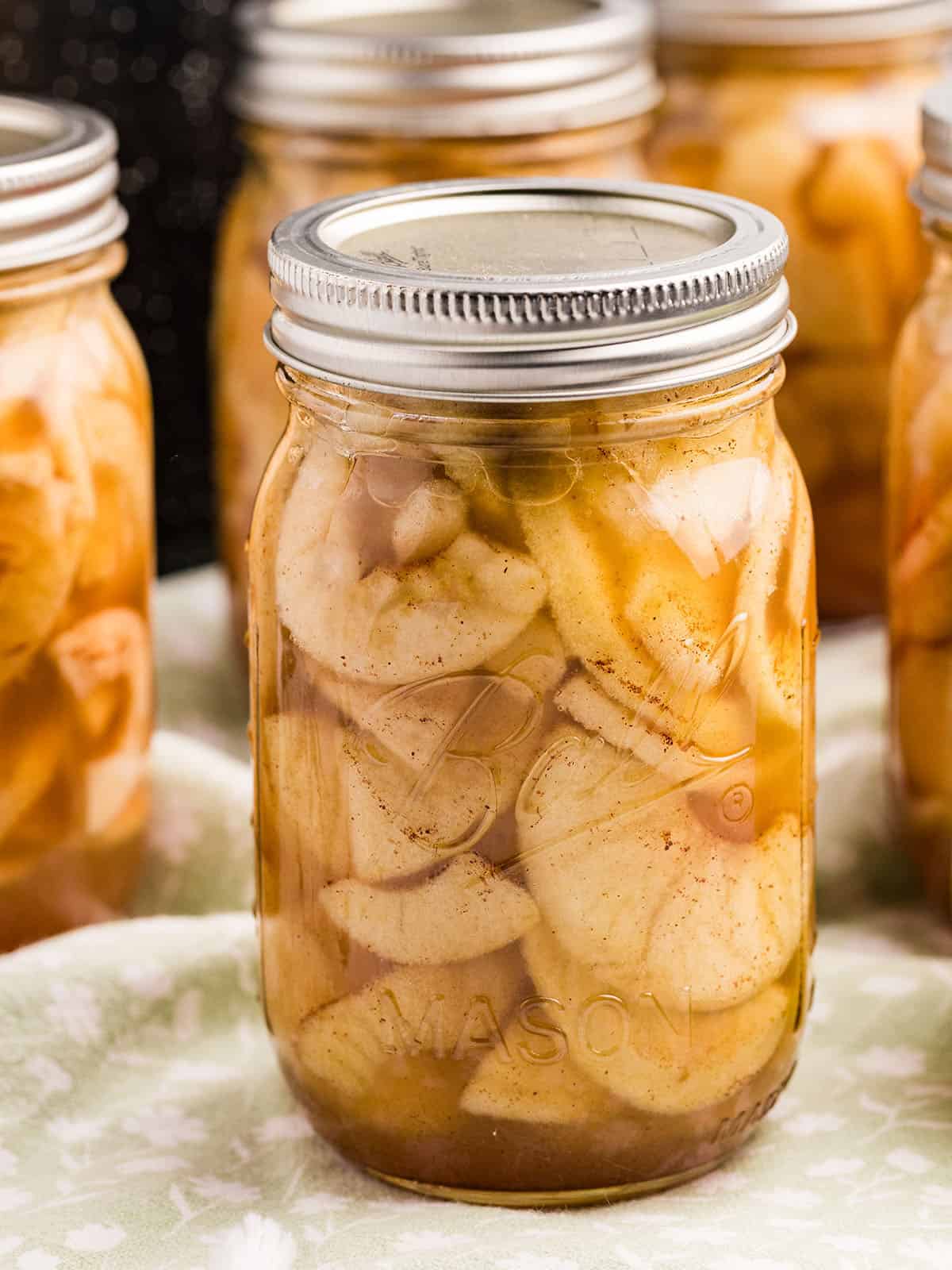 A jar of apple pie filling with several others in the background. 