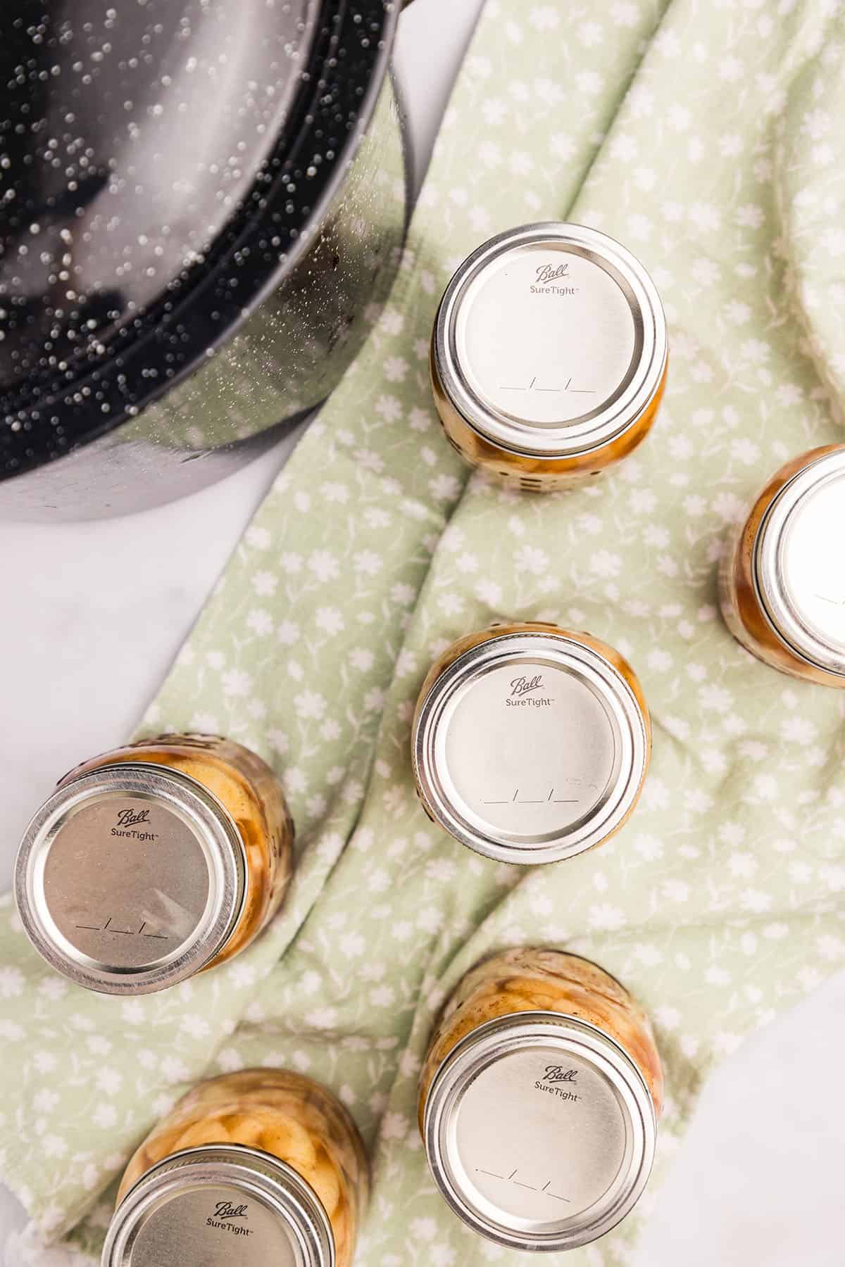 Jars of apple pie filling on a light green cloth, cooling out on the countertop. Top veiw.