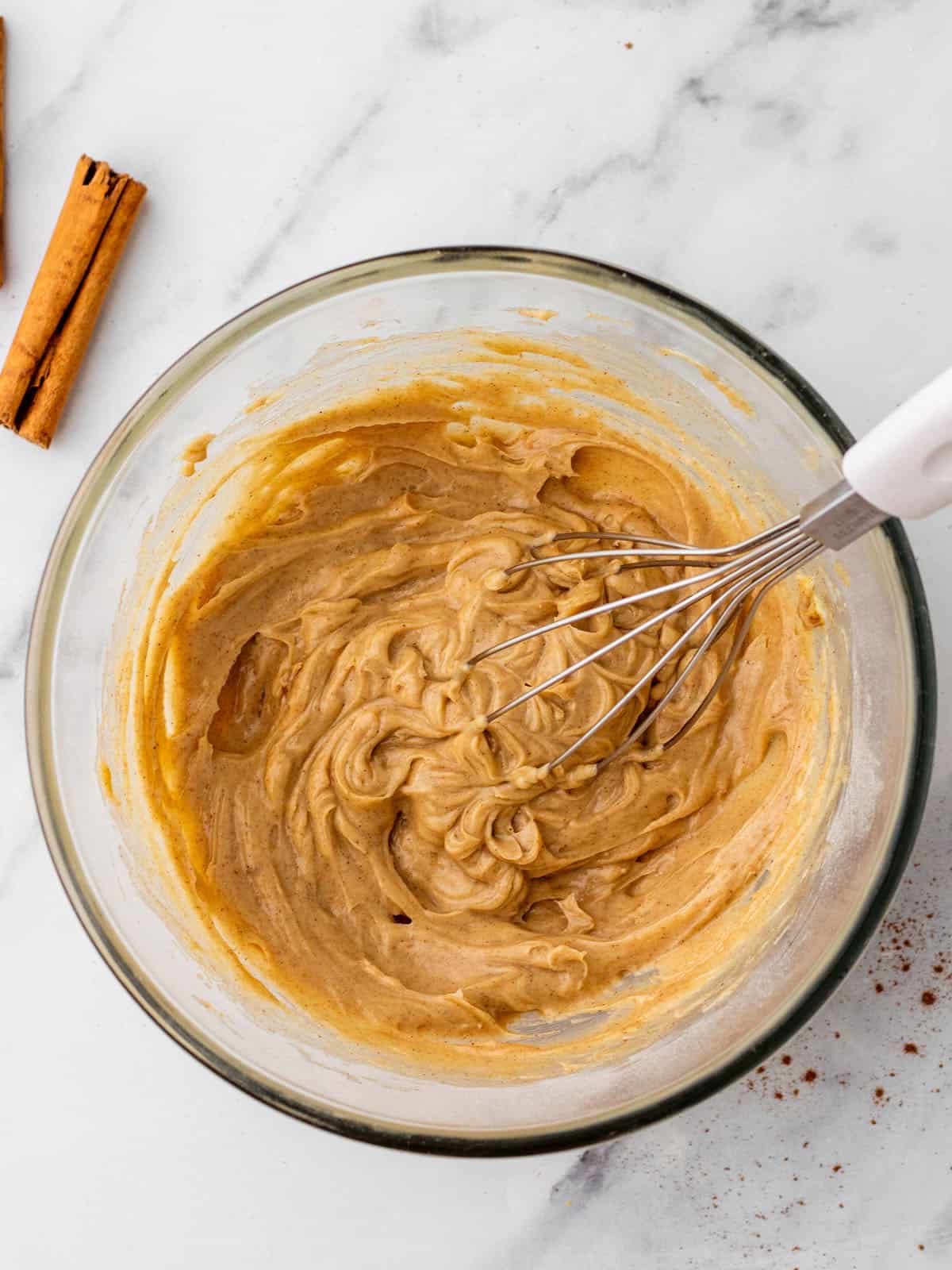 Cinnamon butter being made with a whisk in a clear bowl, top view. 