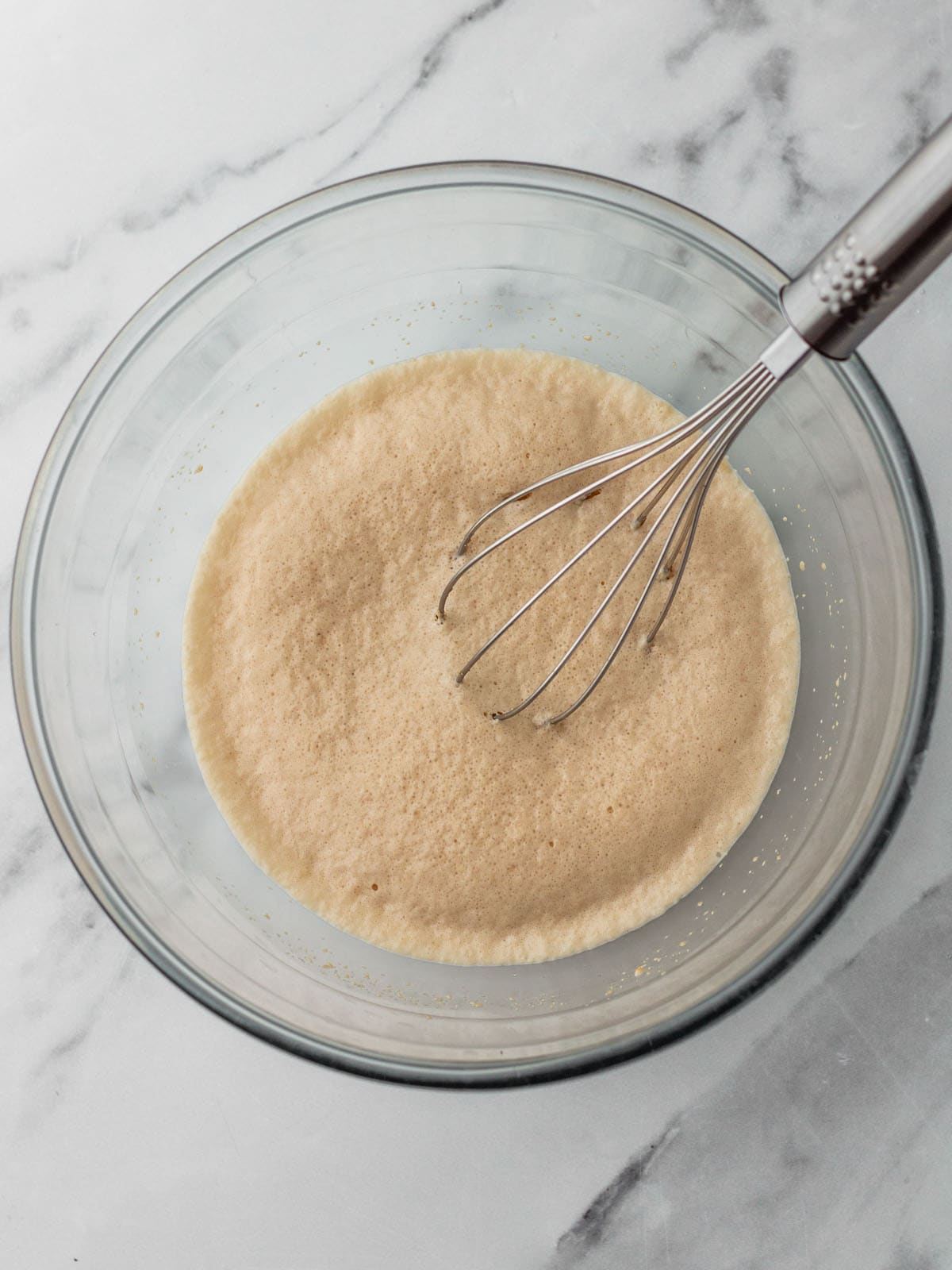 Yeast bloomed in a bowl with milk, with a whisk in it. Top view.