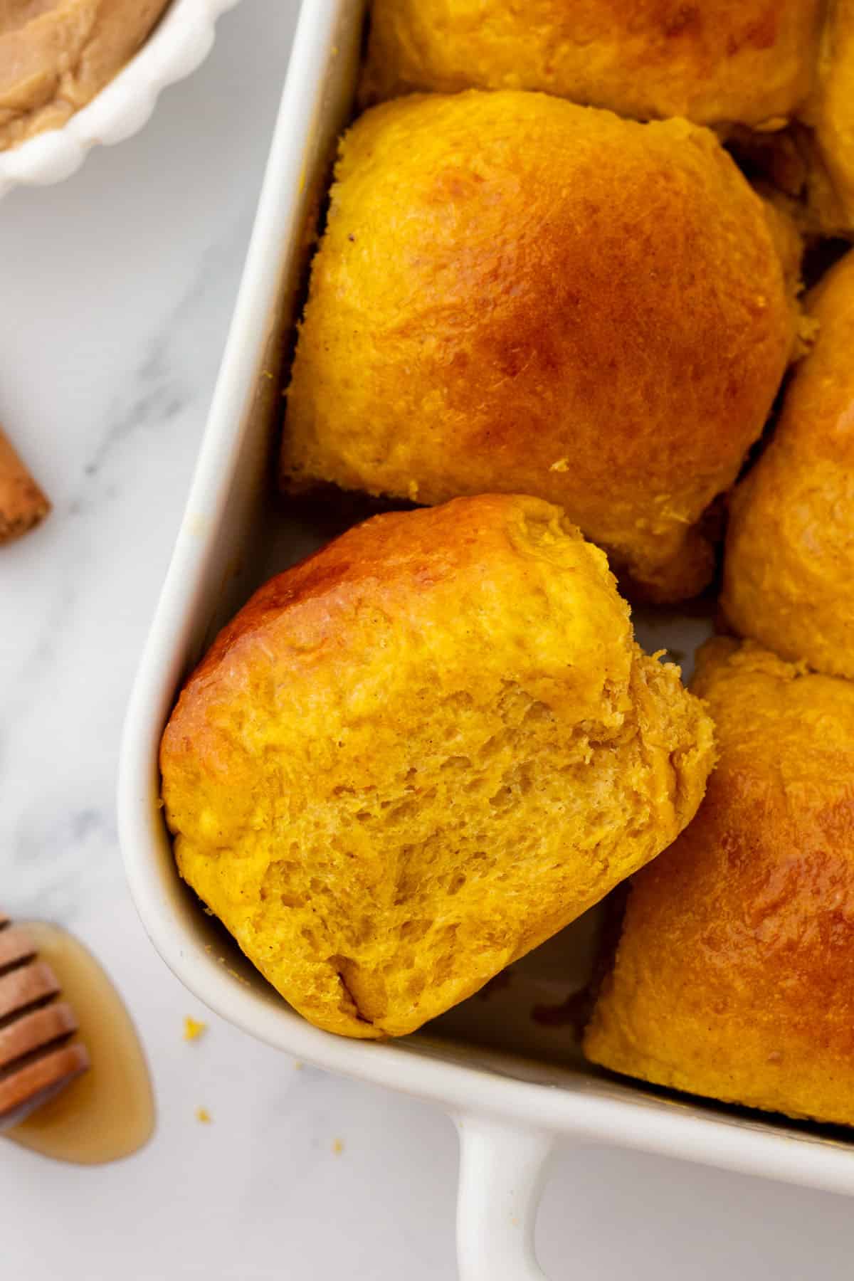 A white baking dish filled with fresh baked pumpkin dinner rolls.