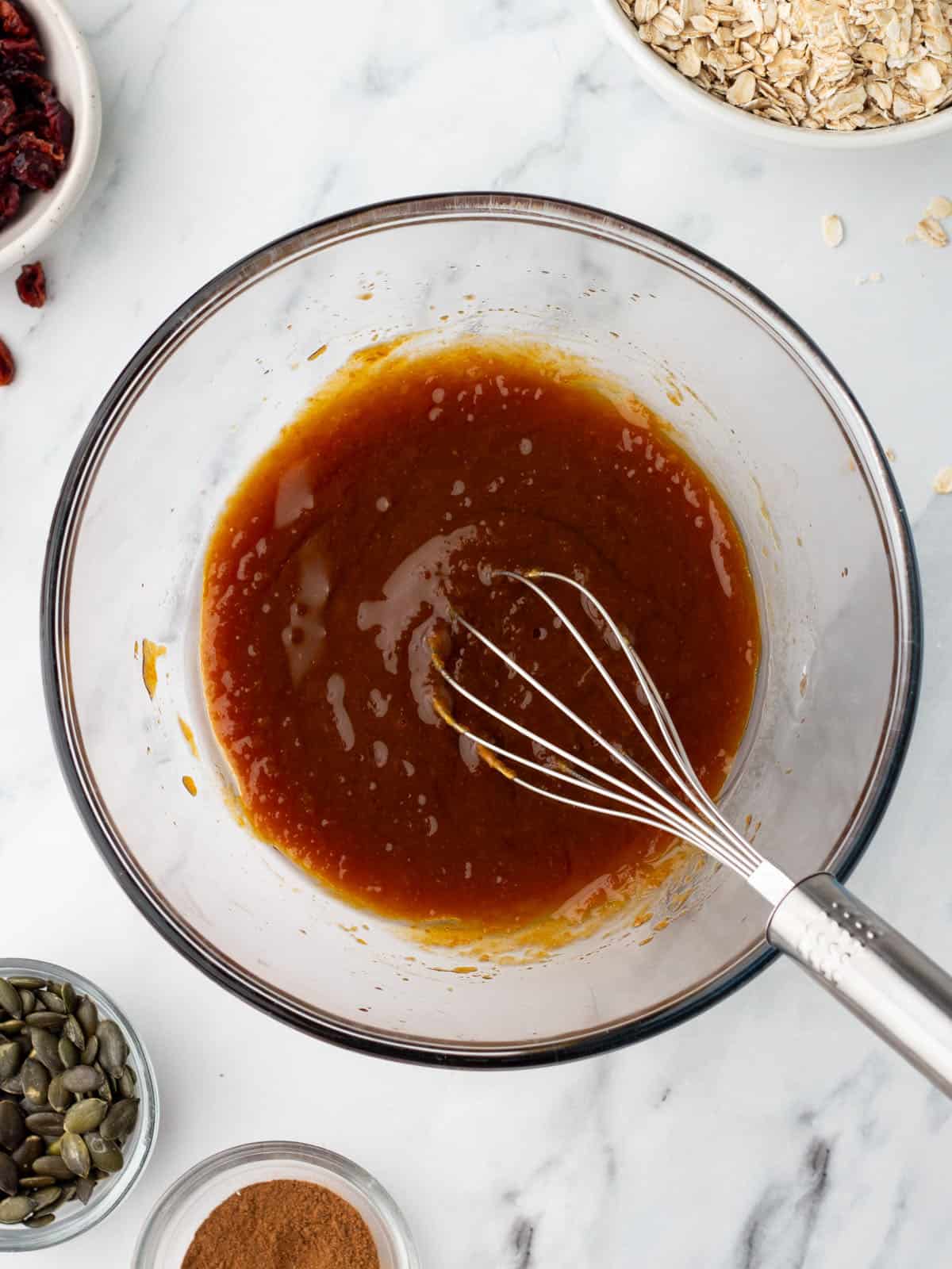 Wet ingredients in a mixing bowl getting stirred with a whisk, top view. 