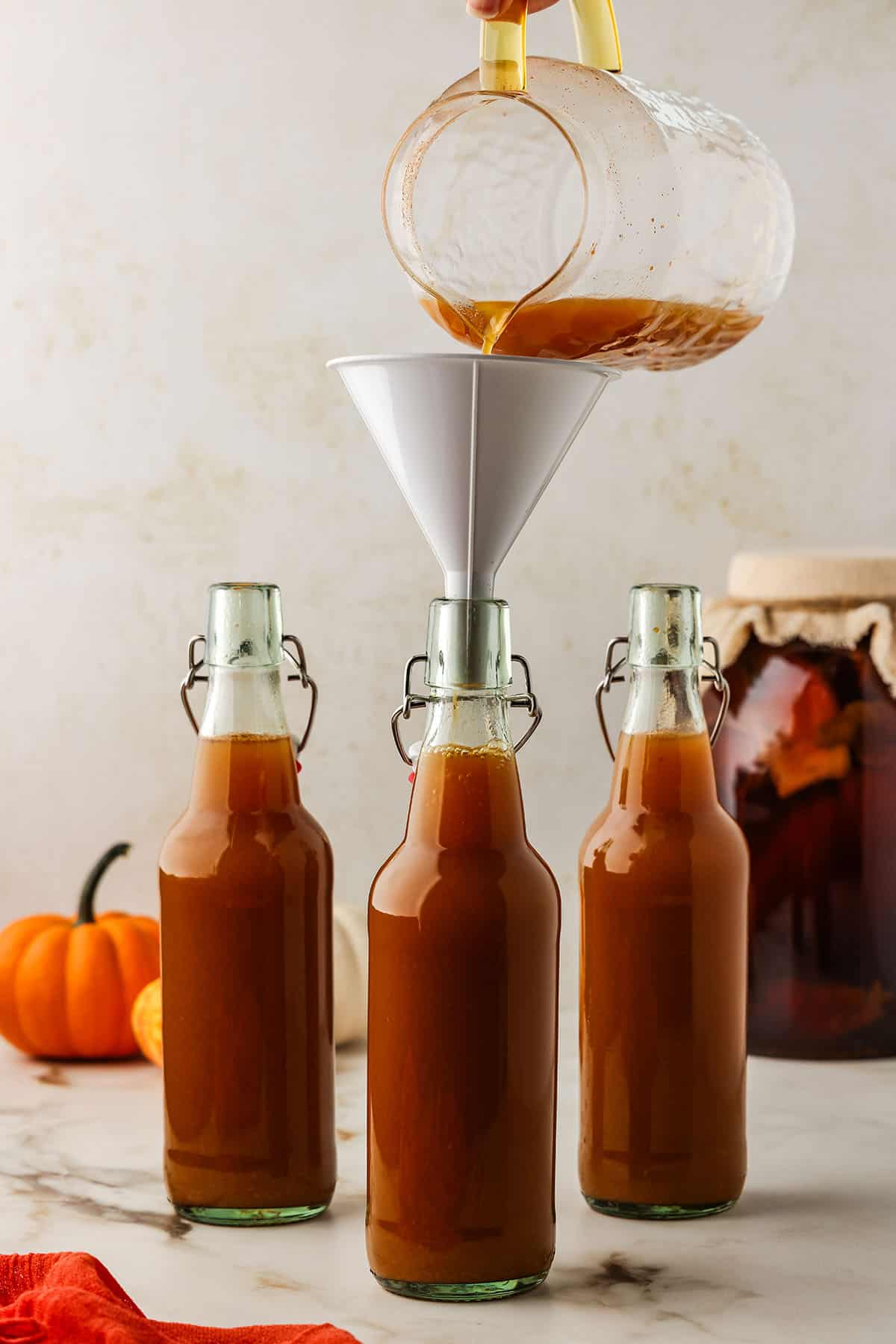 3 flip top bottles of pumpkin kombucha. One has a funnel with kombucha pouring into it. 