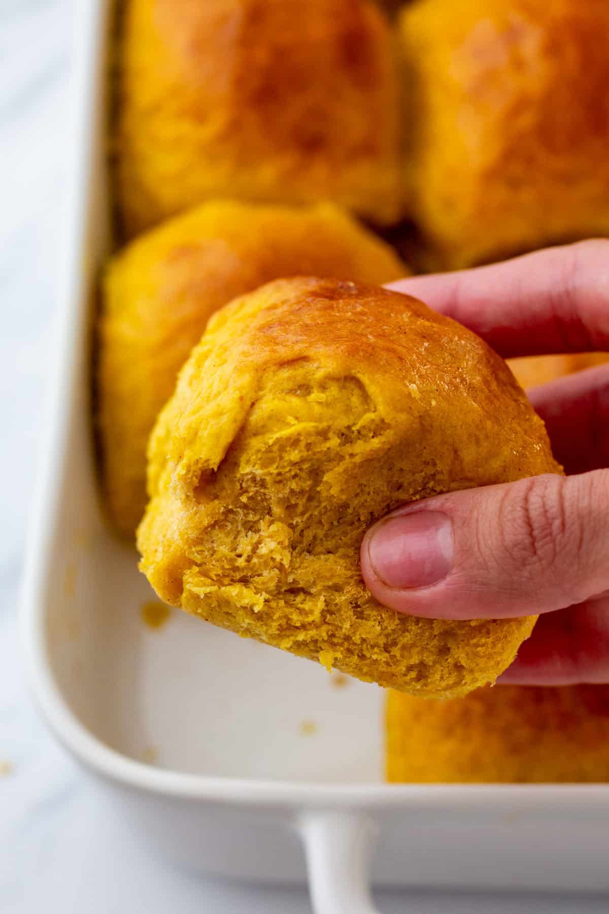 A hand holding a pumpkin dinner roll. 