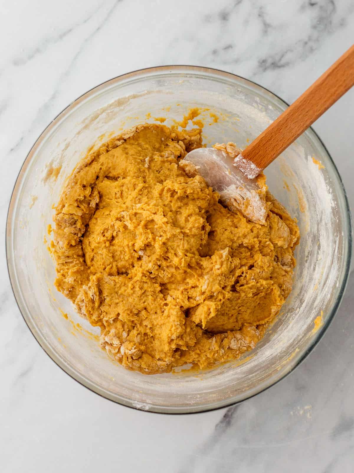 A bowl with pumpkin dough mixed in it, with a wooded spoon resting. Top view. 