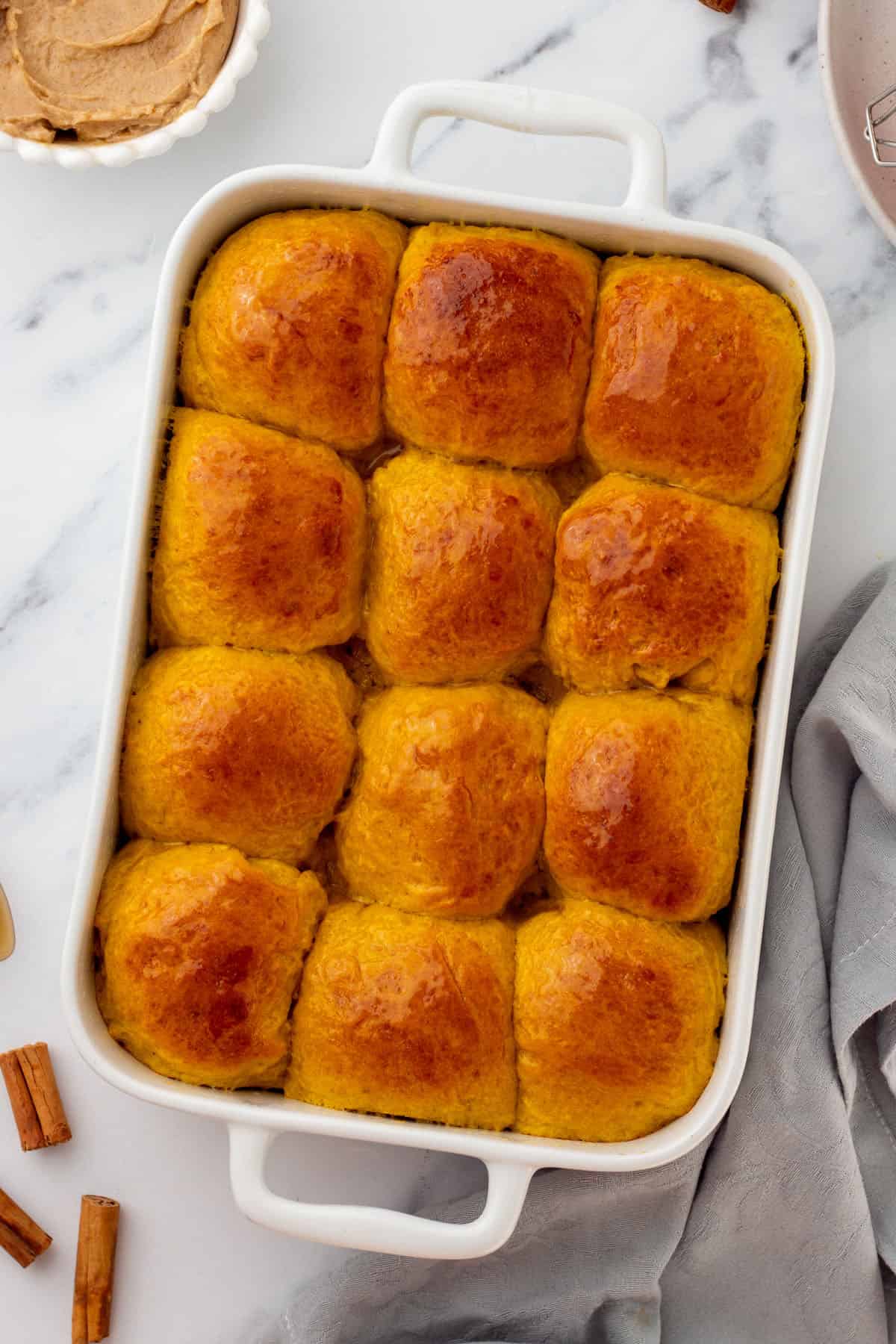 Baked golden pumpkin dinner rolls in a white baking dish, top view. 