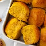 A white baking dish filled with fresh baked pumpkin dinner rolls.