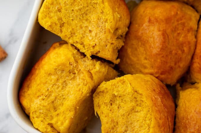 A white baking dish filled with fresh baked pumpkin dinner rolls.