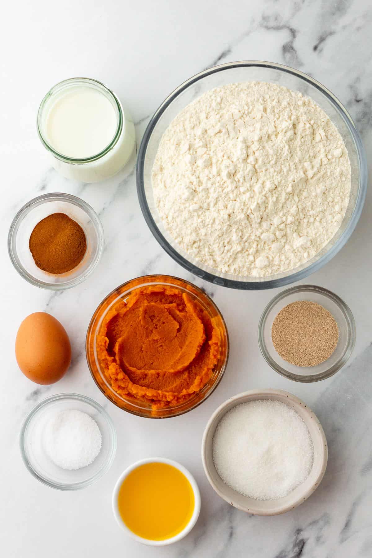 Ingredients for pumpkin dinner rolls in bowls on a white counter, top view. 