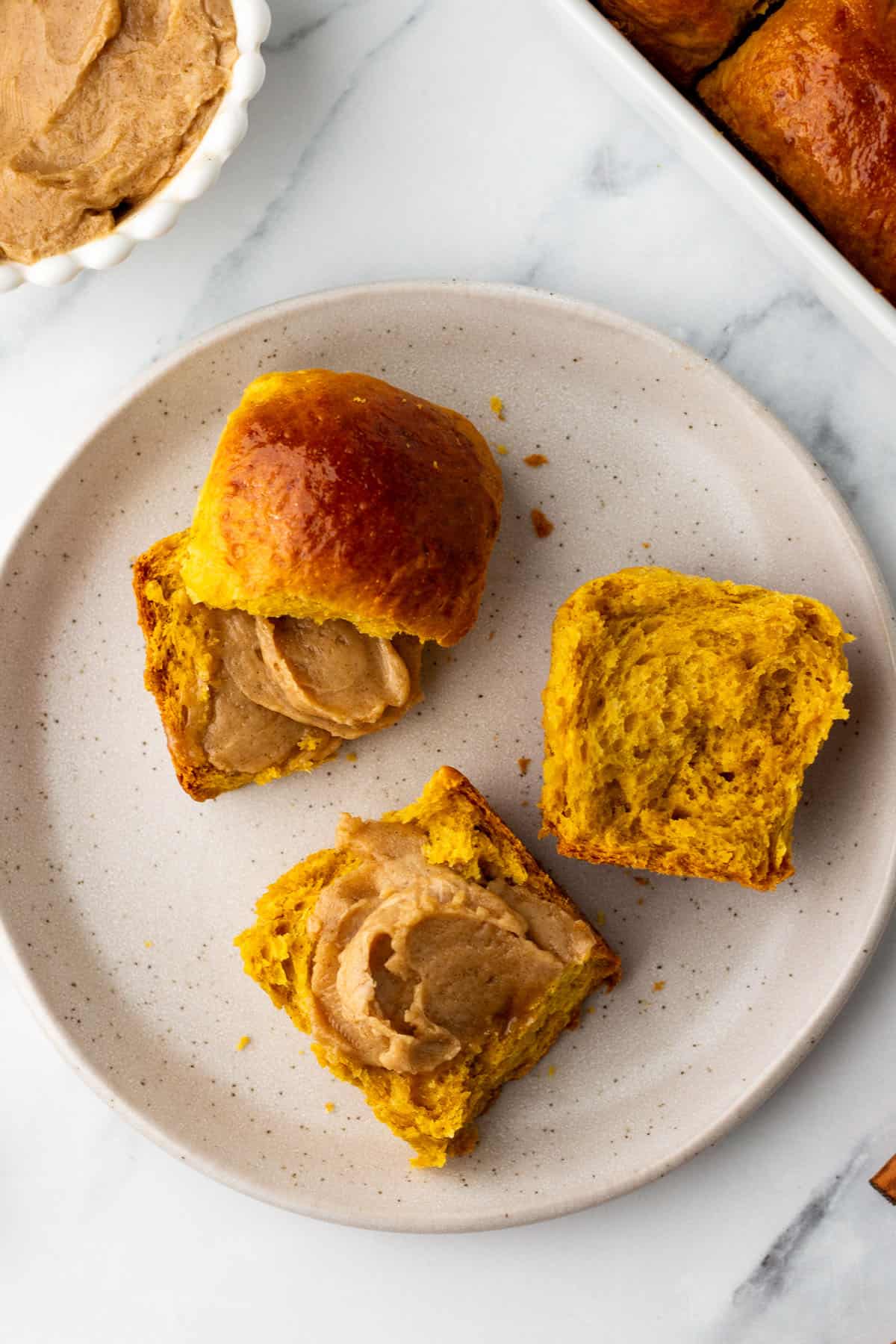 Pumpkin dinner rolls with cinnamon butter on a plate, top view.