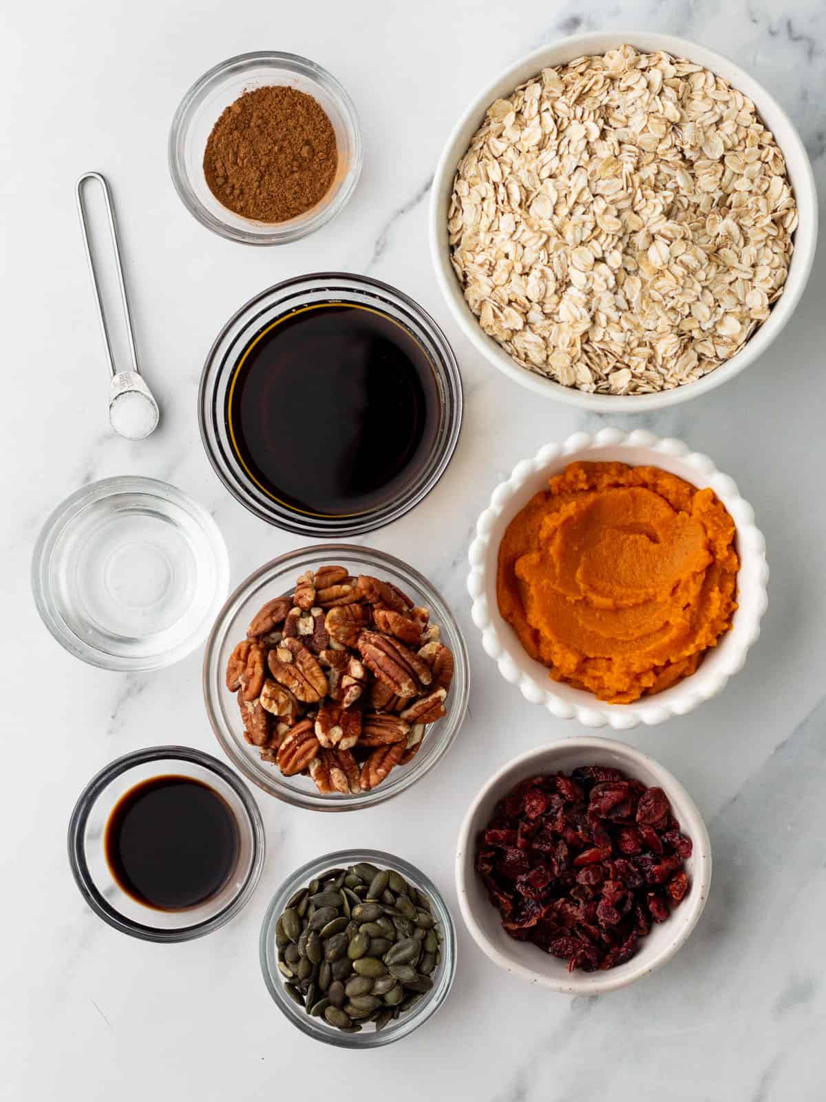 Pumpkin granola ingredients in separate bowls on a white counter, top view. 