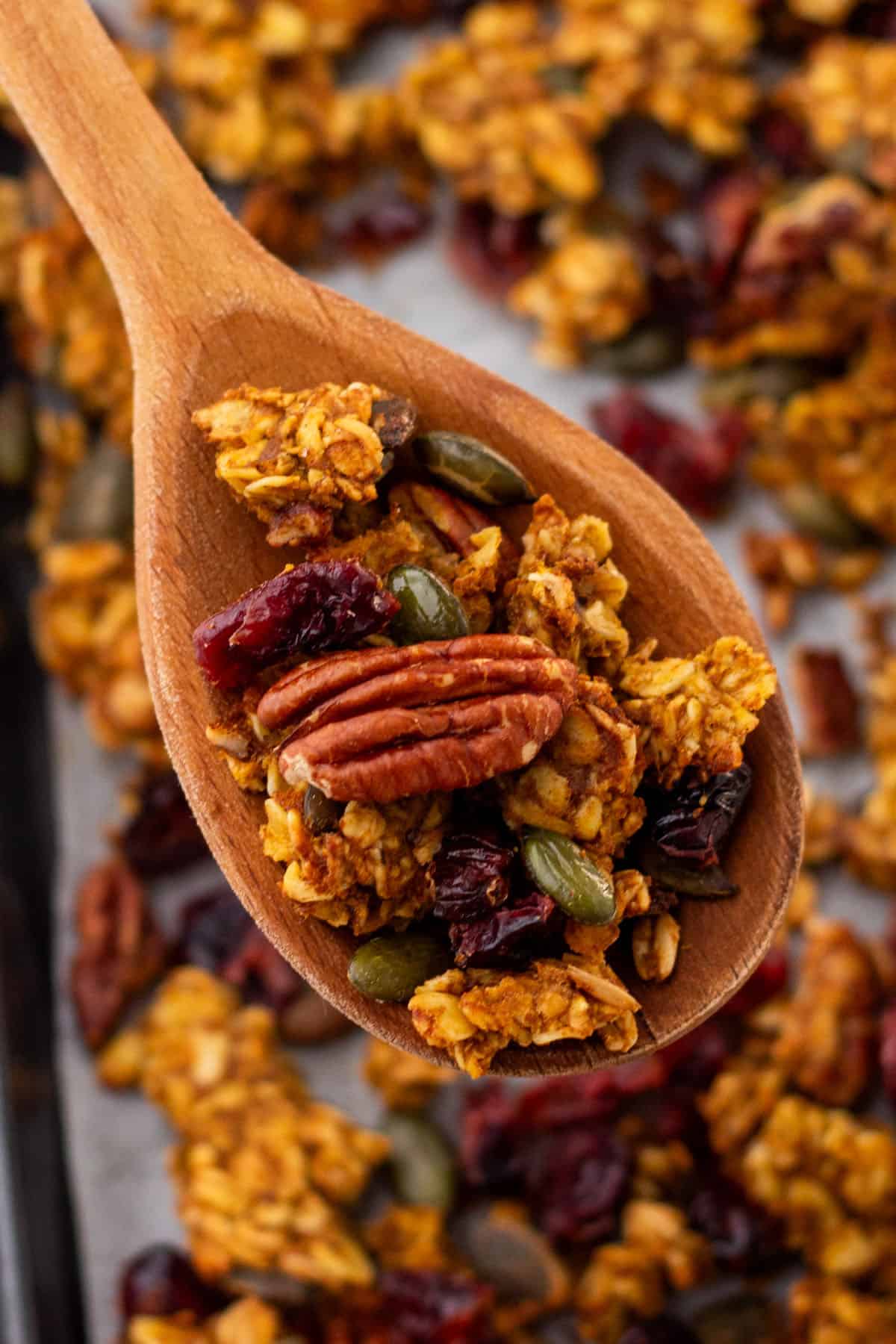 Granola on a wooden spoon being lifted from a sheet pan of freshly baked granola. 