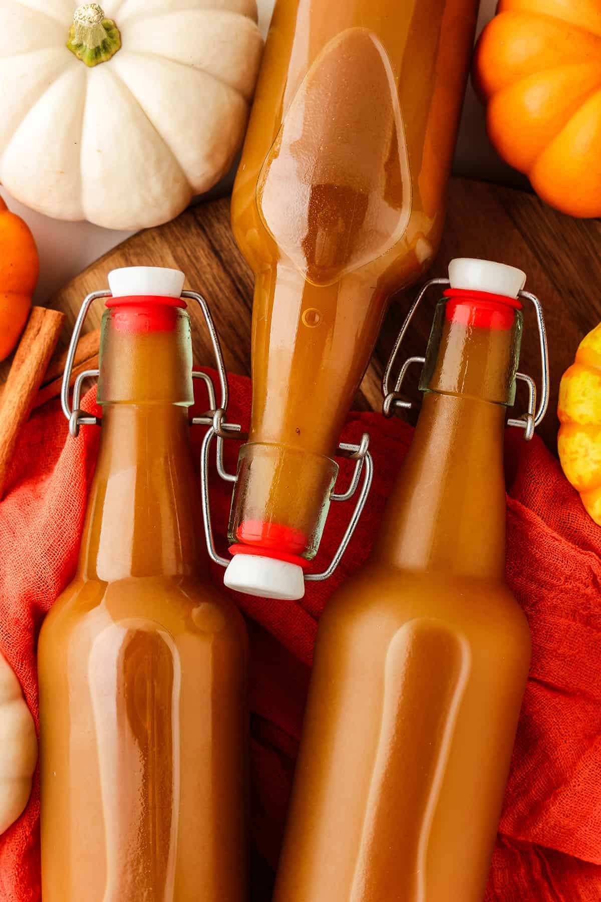 3 bottles of kombucha on their side, surrounded by various colors of pumpkins. 