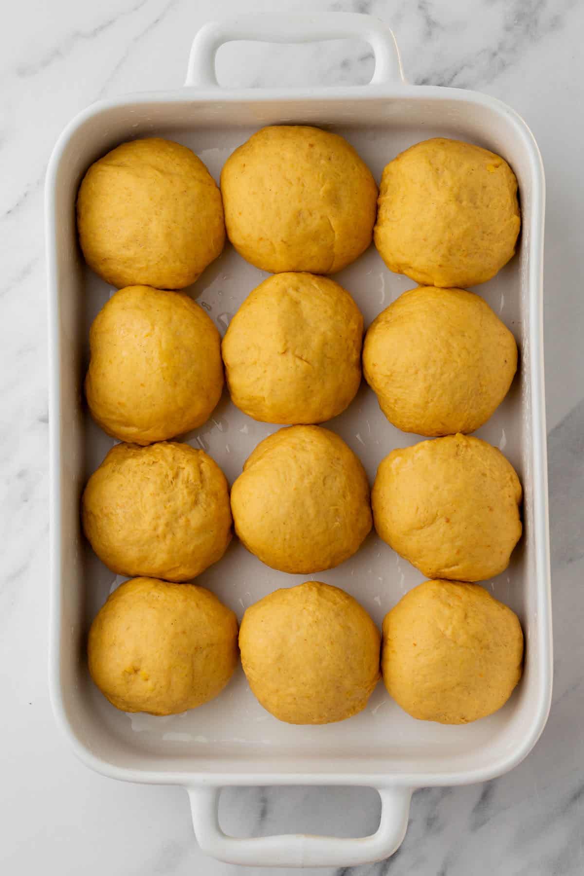 Rolls of pumpkin dough in a white baking pan.