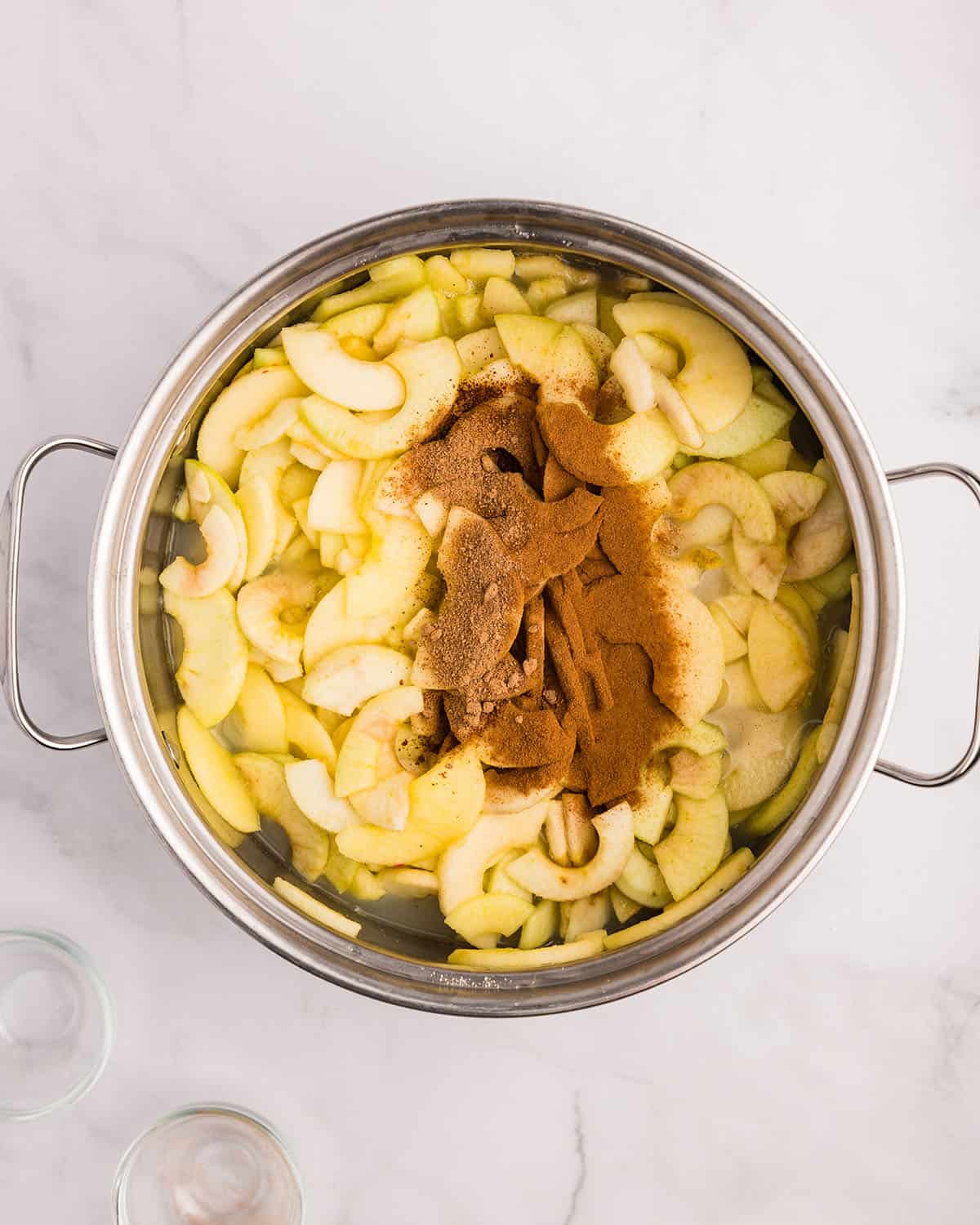 Cooked apples in a pot with spices on top, top view. 