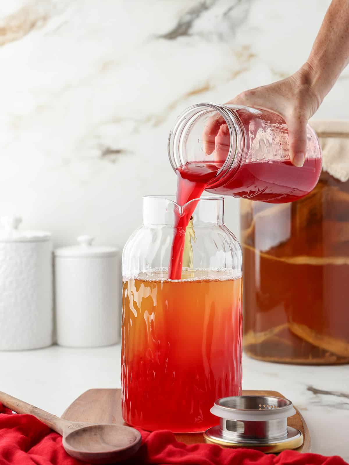 Cranberry kombucha pouring into a large pitcher over regular kombucha.