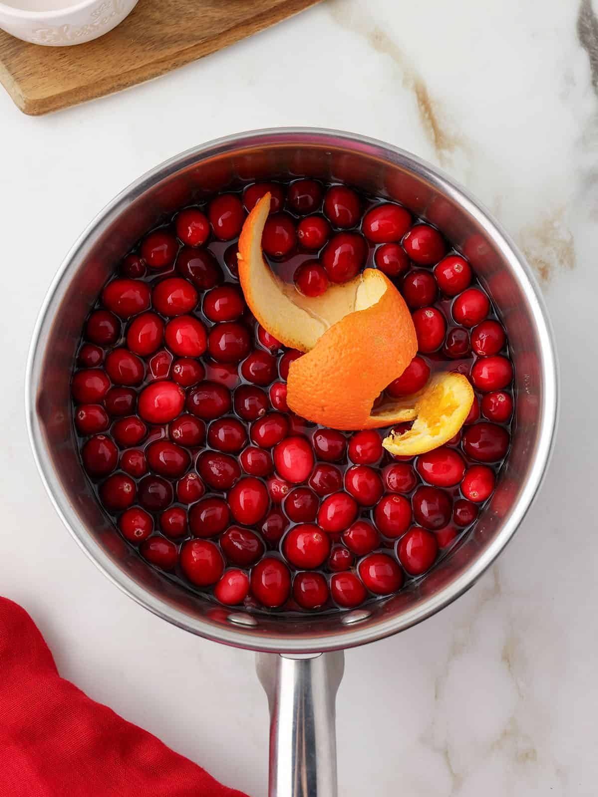 Cranberries and an orange peel in a pot, top view.