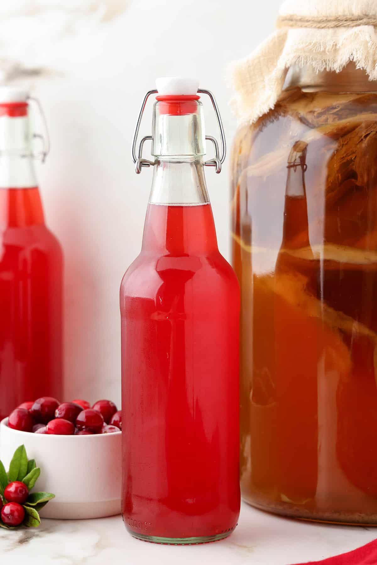 Bottle of cranberry kombucha next to a gallon batch of regular kombucha.